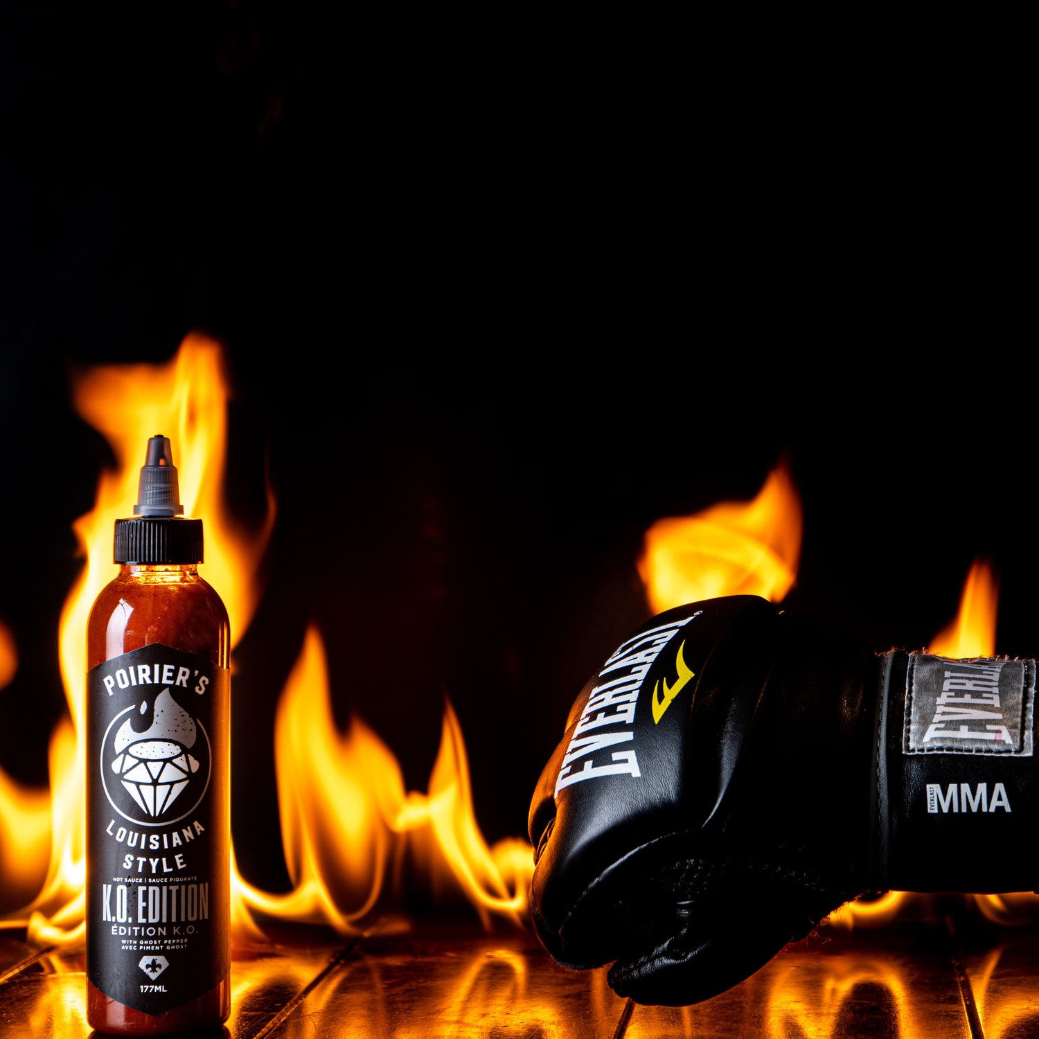 A bottle of hot sauce being punched by a MMA glove  on a fiery background