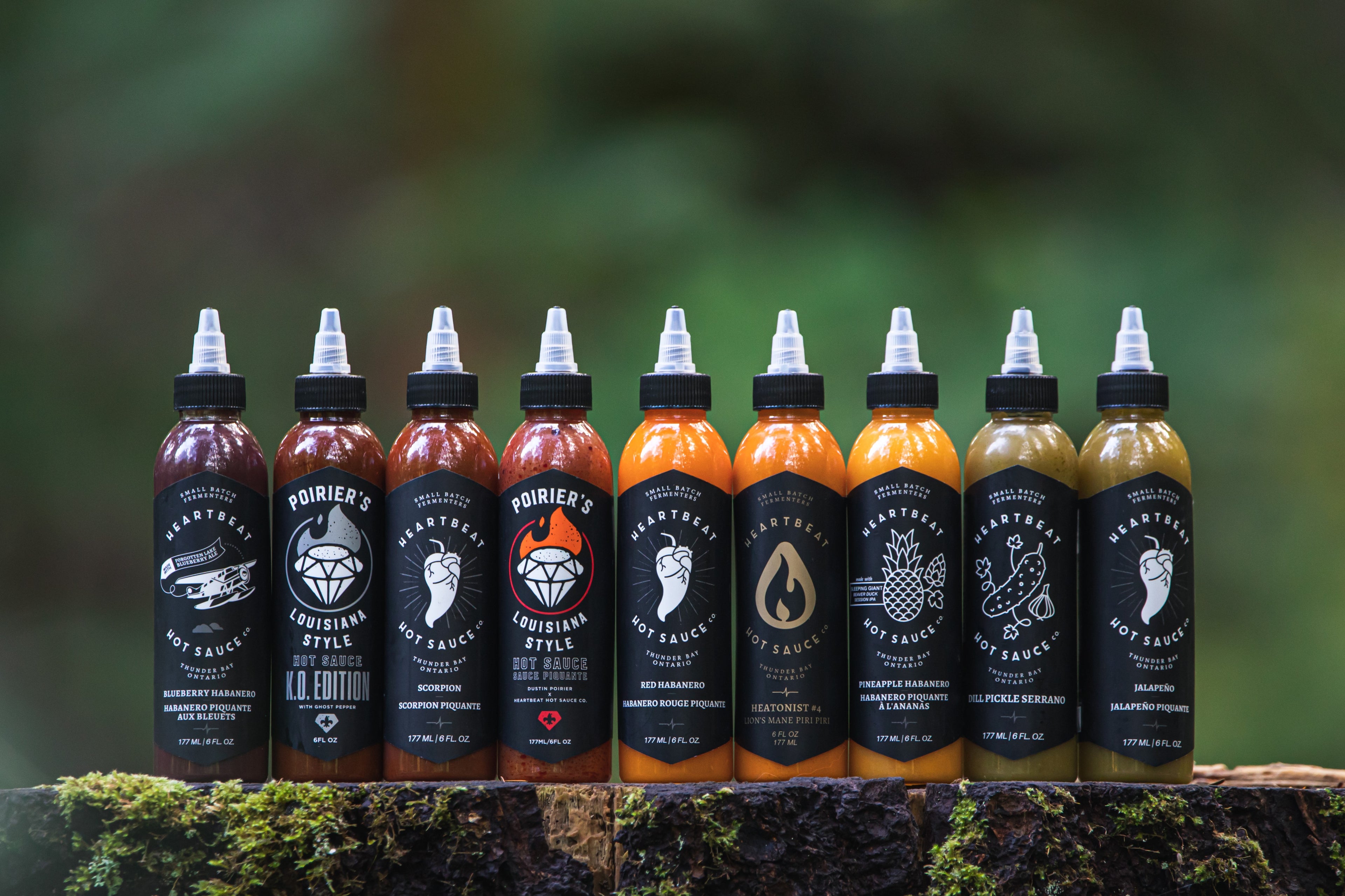 A variety of hot sauces over a tree stump with a blurred forest background